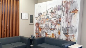 A modern waiting area with a large abstract painting, two grey sofas, a small table, and a marble coffee table. - Hotel Il Gabbiano (Termini Imerese)