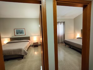 A hotel room with two beds, a bedside table with a lamp, a framed picture on the wall, and a window with curtains.