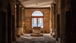 A corridor with arched brick walls, columns, and a large window with decorative glass. - Locanda Ai Santi Apostoli (Venice)