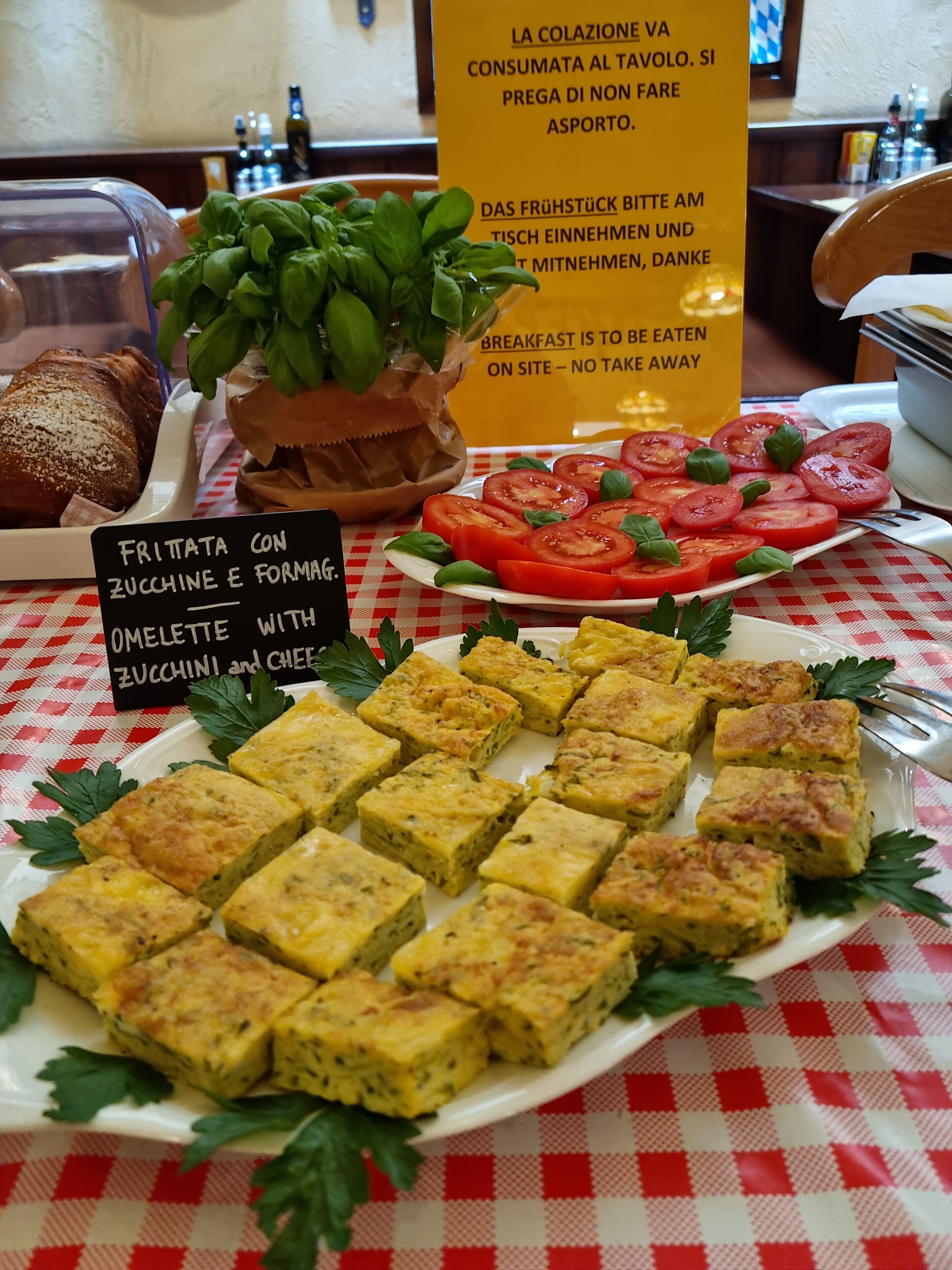 Un buffet de petit-déjeuner proposant divers plats, notamment une omelette aux courgettes et au fromage, des tranches de tomates et du pain.