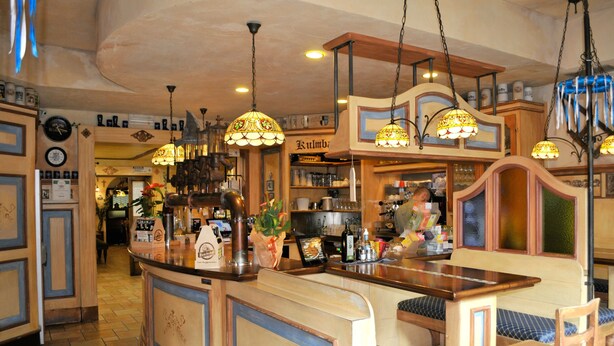 Een bar met houten meubels, hangende lampen en een toonbank met verschillende artikelen.