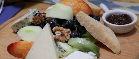 Una tabla de madera con frutas variadas y queso, un cuenco pequeño de mermelada y un vaso de agua.