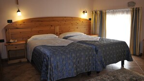 Een slaapkamer met twee bedden, een houten hoofdbord, nachtlampjes en een groot raam met gordijnen.