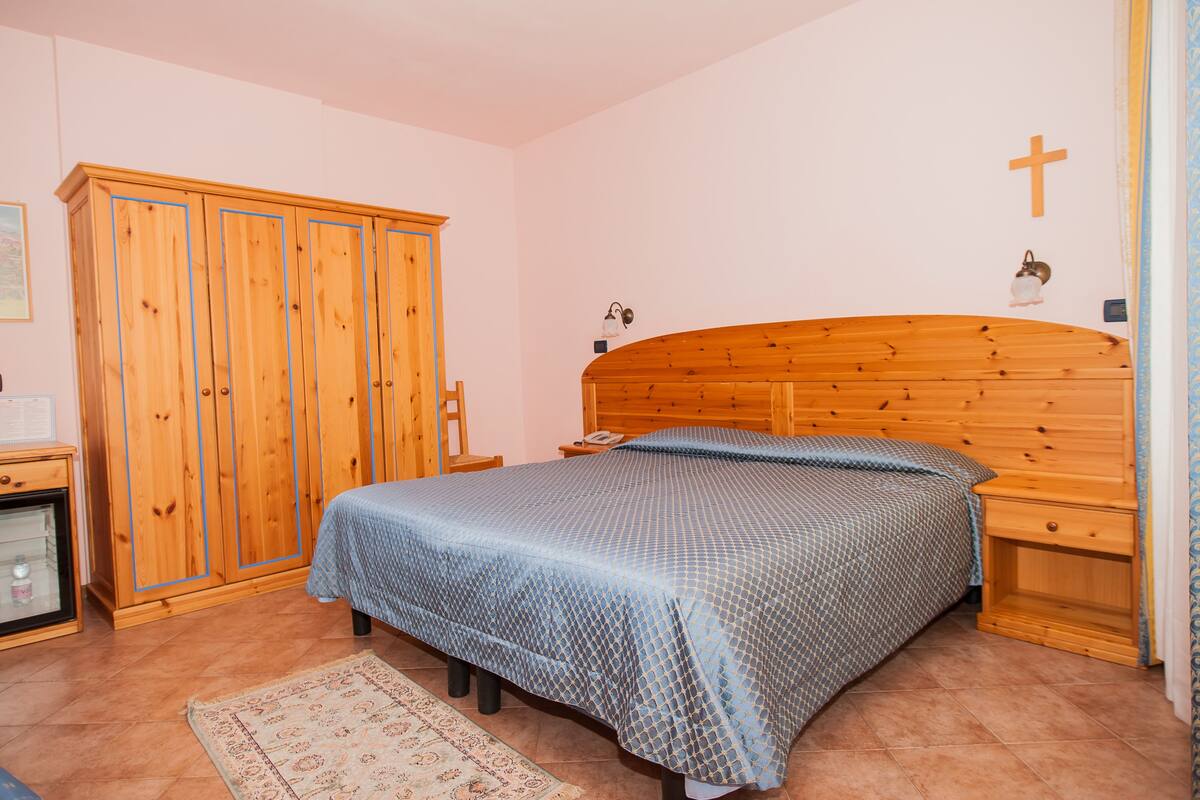 Una camera da letto con un letto di legno, un armadio, un comodino e una croce appesa al muro.