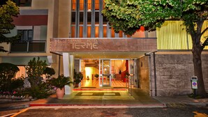The Grand Hotel Terme entrance with a glass door, a staircase, and a landscaped area with plants.
