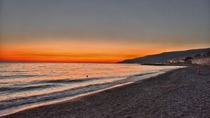 A beach with a sunset, calm sea, and distant hills.