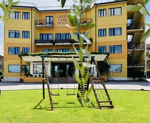 Un hotel de varios pisos con fachada amarilla, un cartel que dice 'GREEN PARK HOTEL' y un acceso cubierto con un arenero al frente.