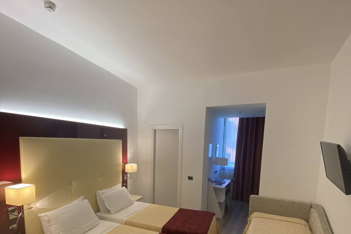 Une chambre d’hôtel avec deux lits, un bureau, une chaise, un téléphone et une porte donnant sur une salle de bain.