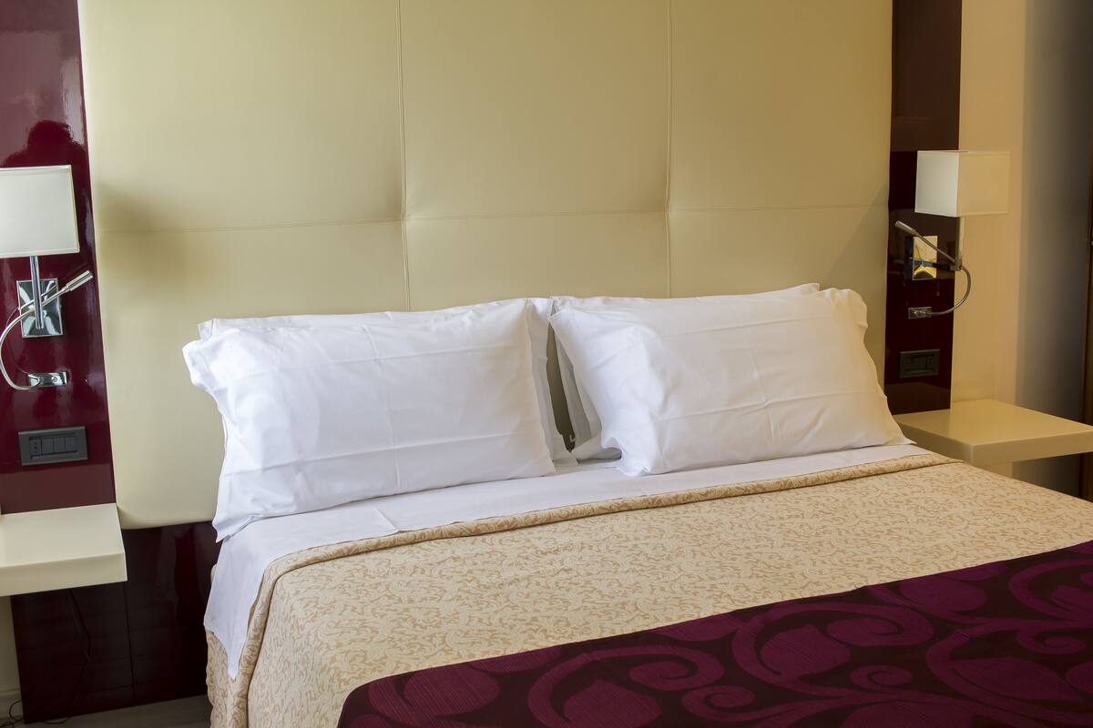 Une chambre d’hôtel avec un grand lit, une tête de lit, deux tables de chevet et une lampe fixée au mur.