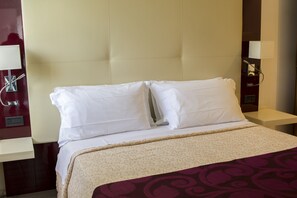 Una habitación de hotel con una cama grande, cabecera, dos mesitas de noche y una lámpara de pared.