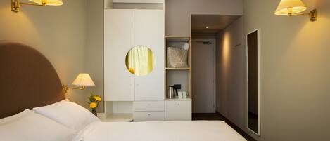 Une chambre d’hôtel comprenant un lit, une armoire, un miroir et deux lampes fixées au mur.