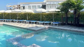 Una piscina con lettini e ombrelloni, un edificio a tema nautico e un siepe curata.