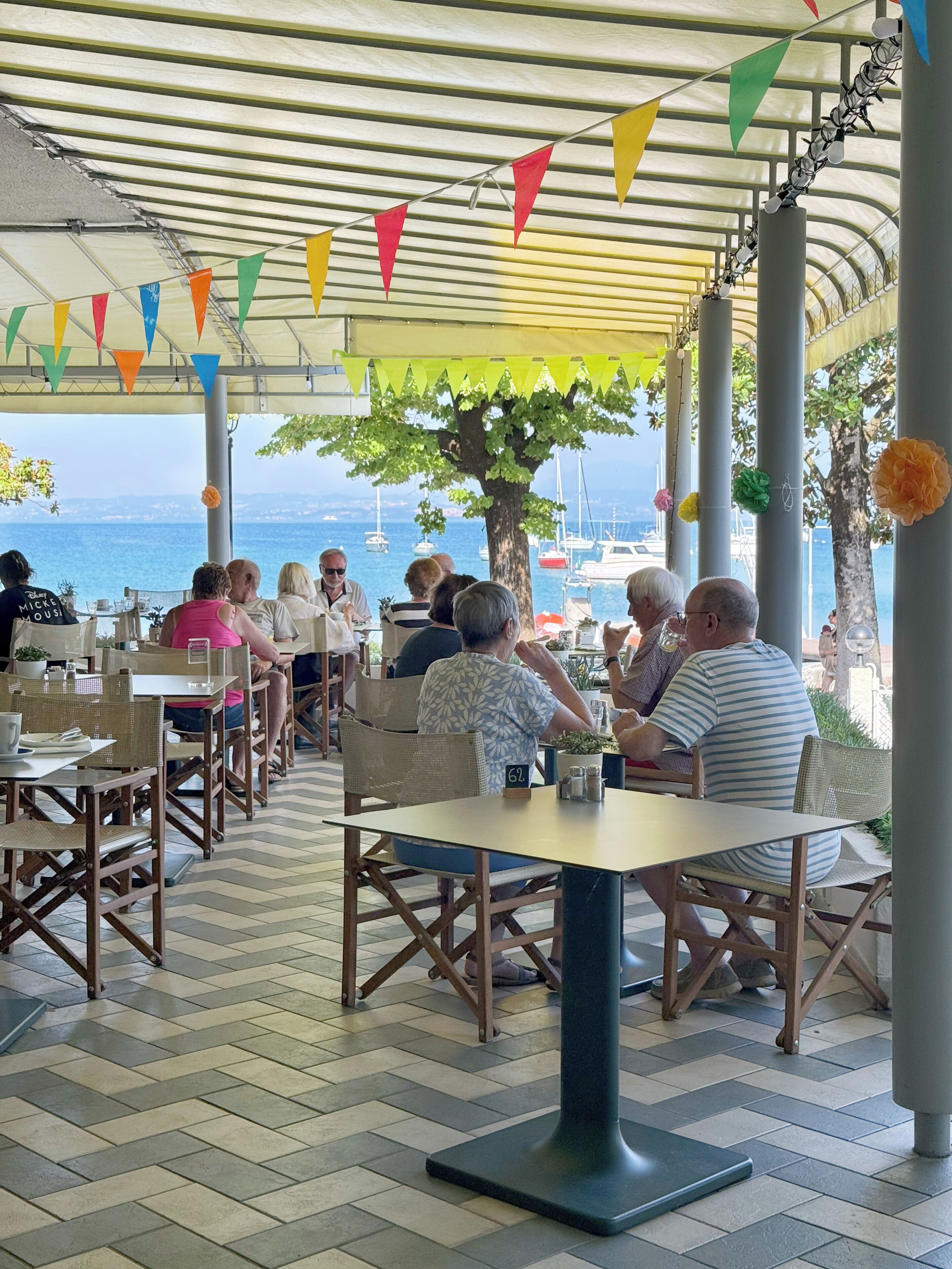 An outdoor seating area with tables and chairs, a view of the sea, and colorful flags.