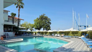 Una piscina con sillones de playa y sombrillas, un área de bar y un edificio con techo rojo.