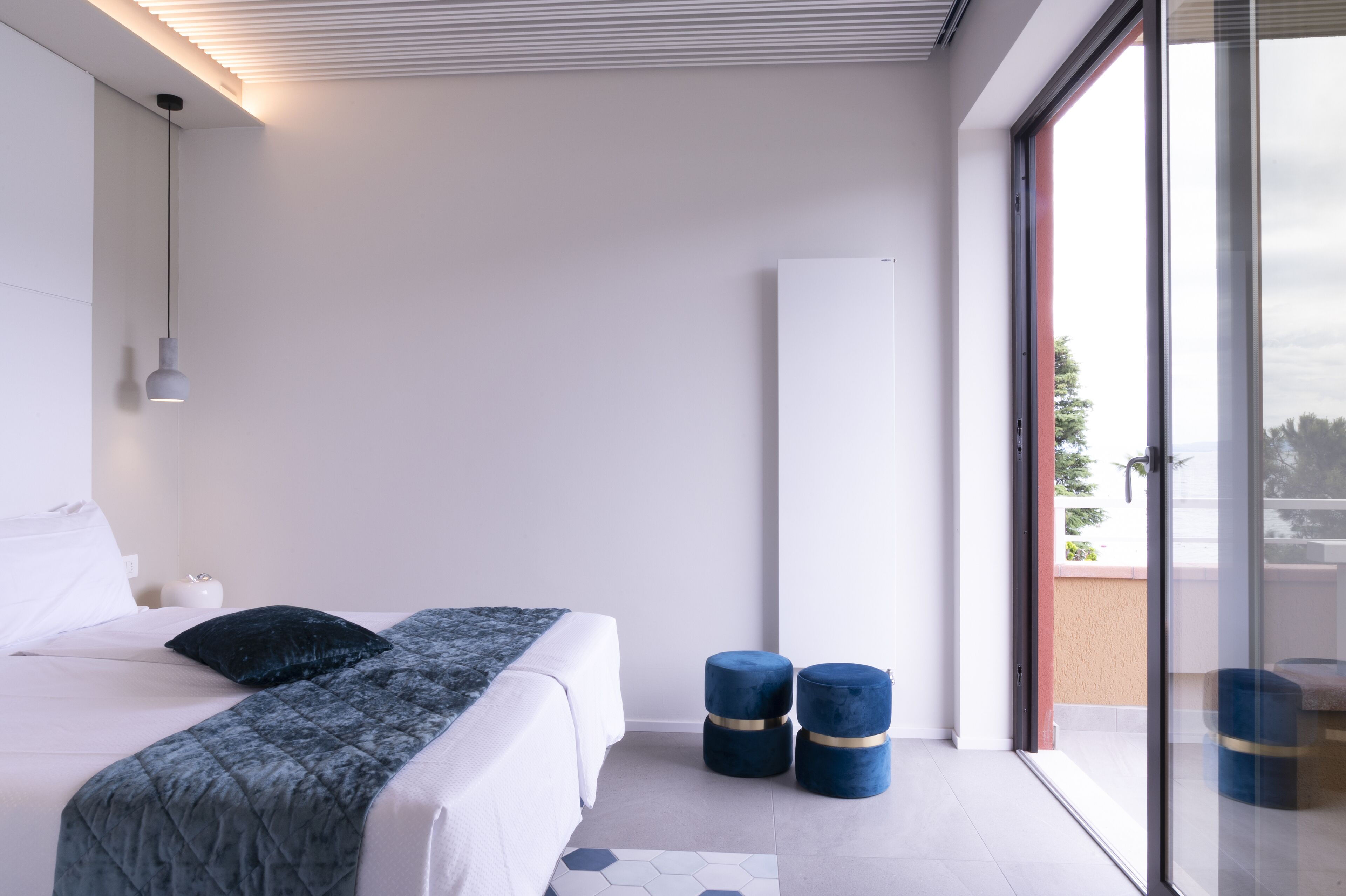 Una camera da letto moderna con un letto grande, un comodino, una lampada a sospensione e vista panoramica attraverso una porta di vetro.