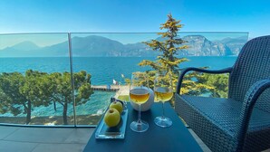 Ein Balkon mit Tisch, gedeckt mit zwei Weingläsern und drei Äpfeln, mit Blick auf eine malerische Küstenlandschaft mit Bergen und Meer.