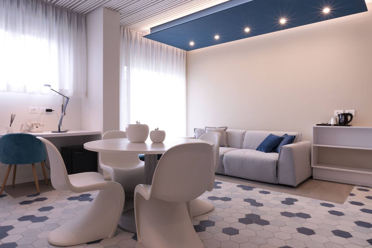 Una sala de estar moderna con una mesa de comedor redonda, sillas blancas, un sofá gris y una estantería.
