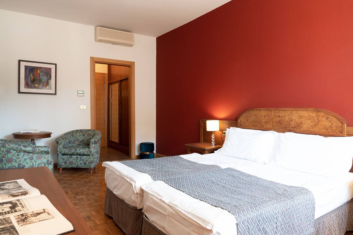 Habitación de hotel con cama, dos sillas, una mesa, una lámpara y un cuadro en la pared.