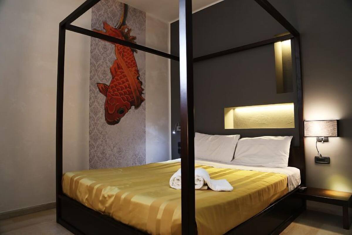 Een hemelbed met een gele en witte streepdeken, een wit kussen en een netjes opgevouwen handdoek op het bed.