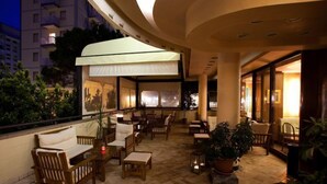 An outdoor lounge area with wooden furniture, potted plants, and a white umbrella providing shade. - Hotel Santa Lucia (San Michele al Tagliamento)