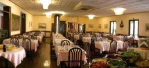 A large dining hall with multiple round tables covered with white tablecloths, arranged in rows.