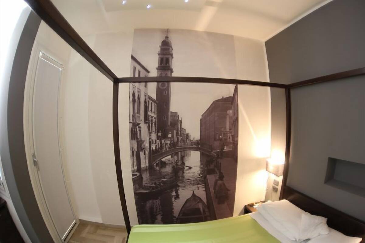Hotelkamer met een bed, nachtkastje, wandtelevisie en een groot stadslandschap op de muur.