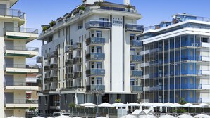 A multi-story hotel with balconies, outdoor seating, and a clear blue sky. - Hotel Byron Bellavista (Jesolo)