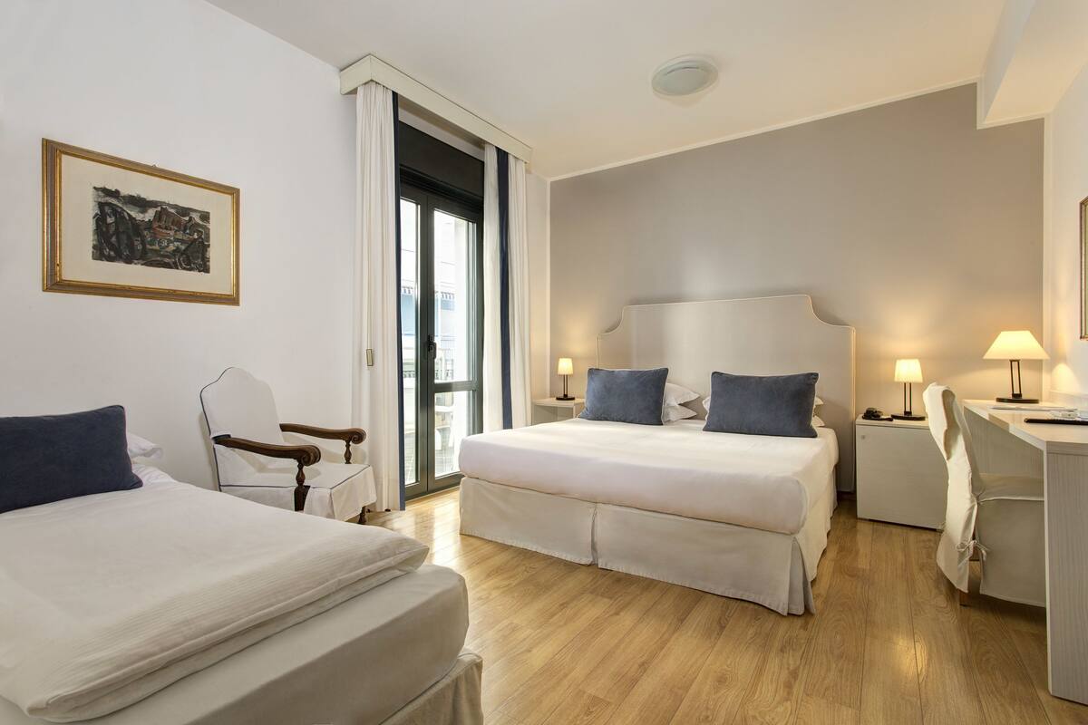 A hotel room with two beds, a desk, a chair, and a window with curtains.