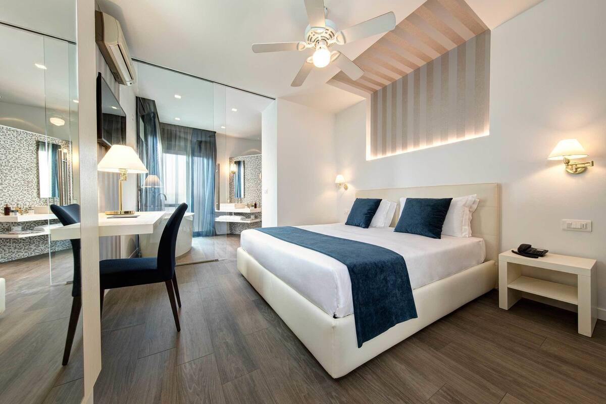 A modern hotel room with a large bed, a desk, and a chair.