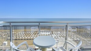 A balcony with a round table and chairs, overlooking a beach with umbrellas and lounge chairs. - Hotel Byron Bellavista (Jesolo)