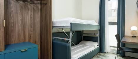 A bunk bed with a desk and chair, a wardrobe with hanging clothes, and a window with curtains.