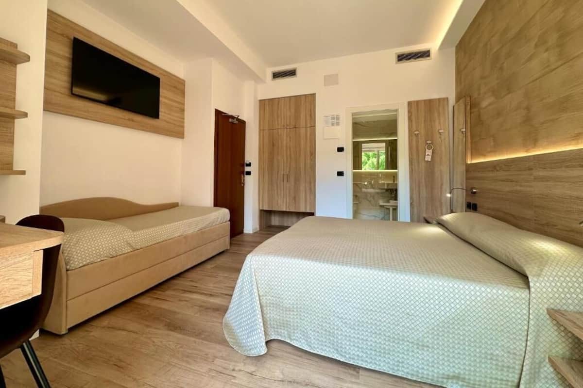 A bedroom with a bed, a desk, and a television mounted on the wall.