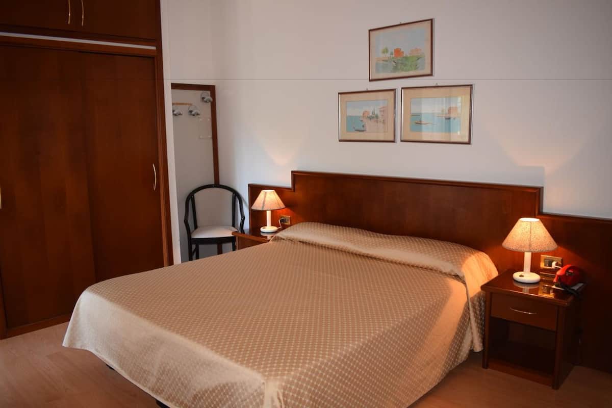 A hotel room with a large bed, two bedside tables with lamps, a wooden wardrobe, and three framed pictures on the wall.