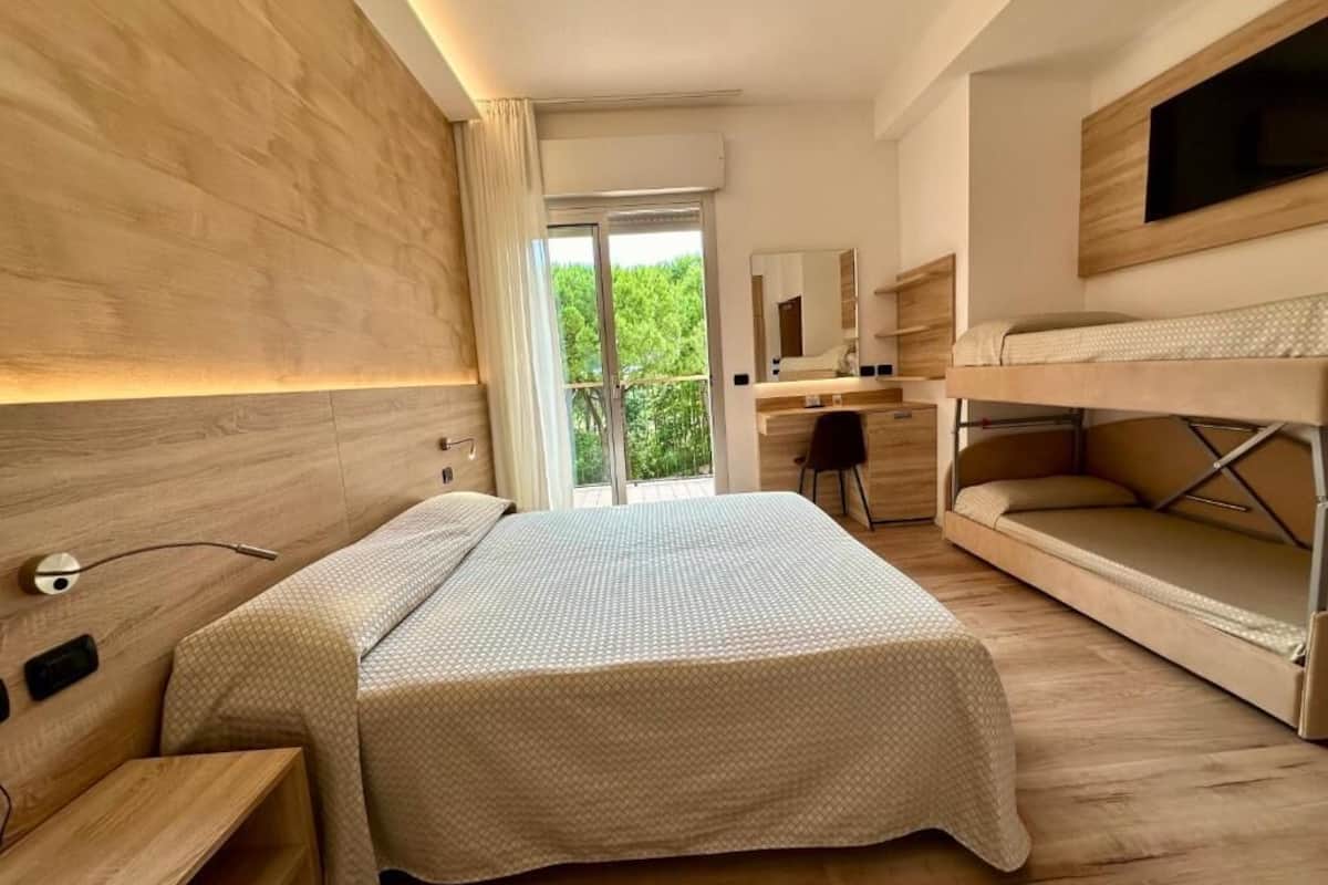 A modern hotel room with a large bed, a desk, and a bunk bed.