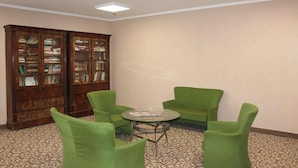 A room with a large wooden bookshelf, green chairs, a small round table, and patterned carpet. - Hotel Salaria (Rome)
