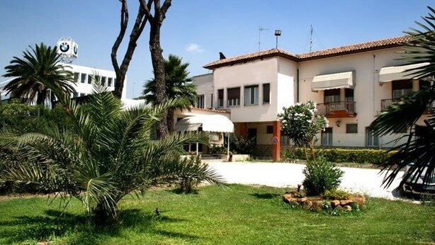 A two-story building with a tiled roof, surrounded by a well-maintained garden with palm trees and a small pond. - Hotel Salaria (Rome)