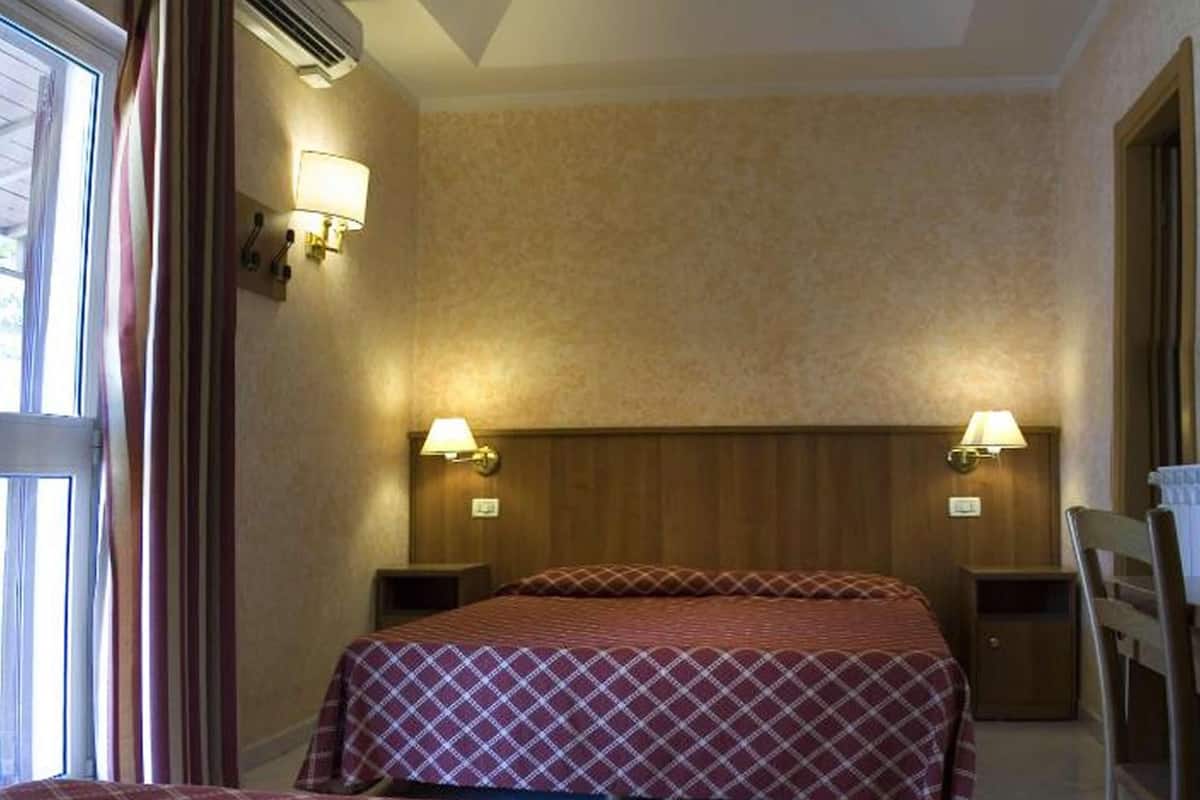 A hotel room with two beds, wooden headboard, two bedside lamps, a wooden nightstand, and a chair.