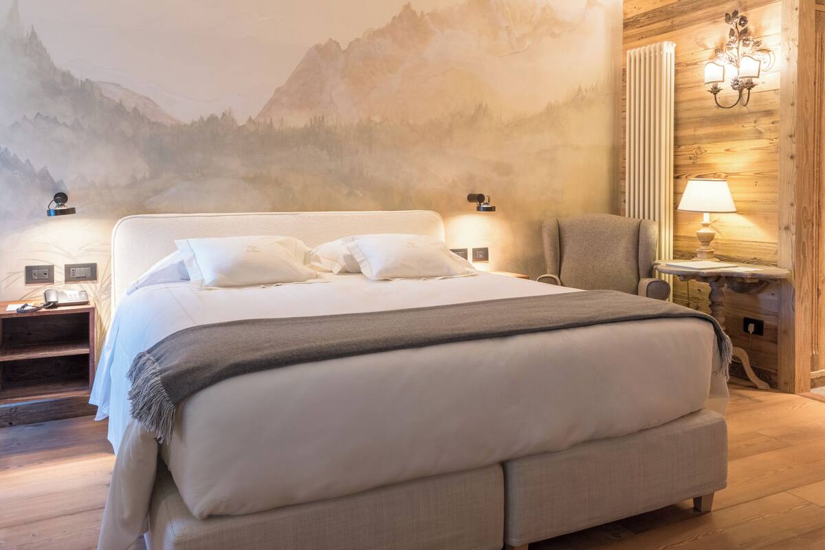 Un dormitorio con una cama grande, una mesita de noche, una silla y una lámpara de pared.