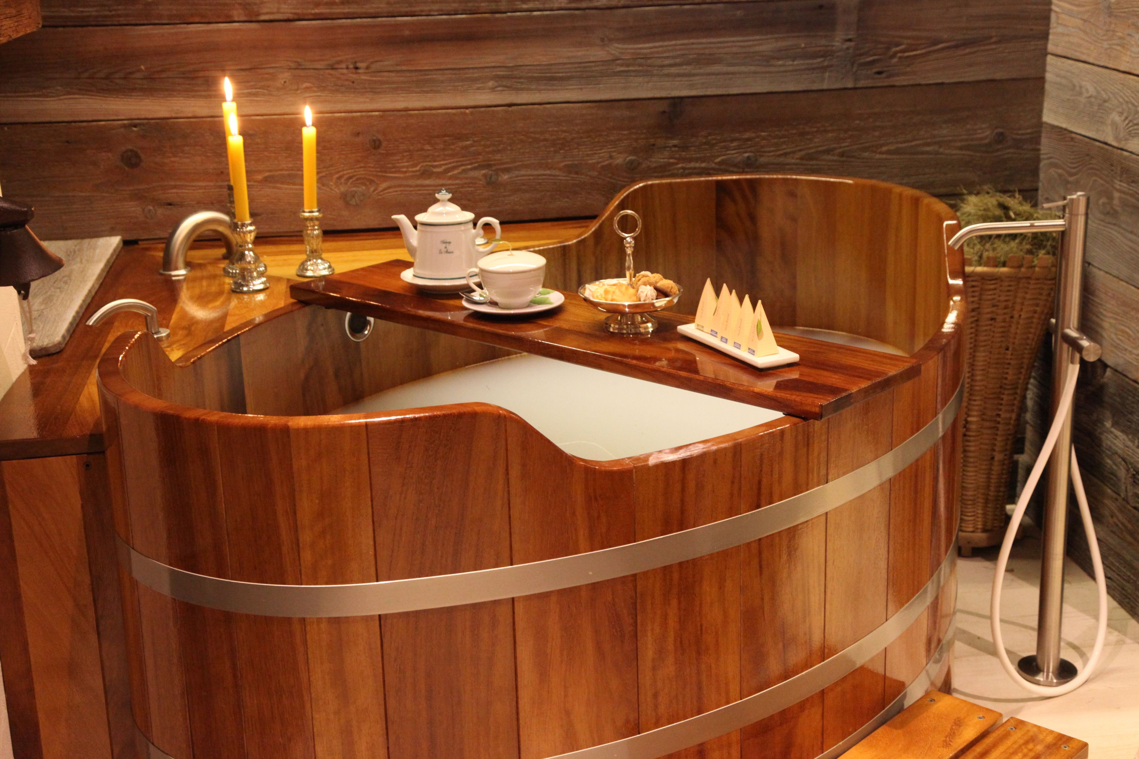 Una bañera de madera con un lavamanos, velas, un hervidor y una bandeja con galletas.