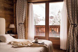 A wooden cabin room with a bed, a nightstand, a lamp, and a window with curtains.