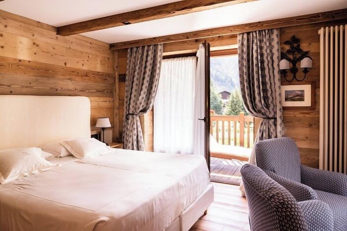 Una habitación con paneles de madera, una cama, una silla y un balcón con cortinas.