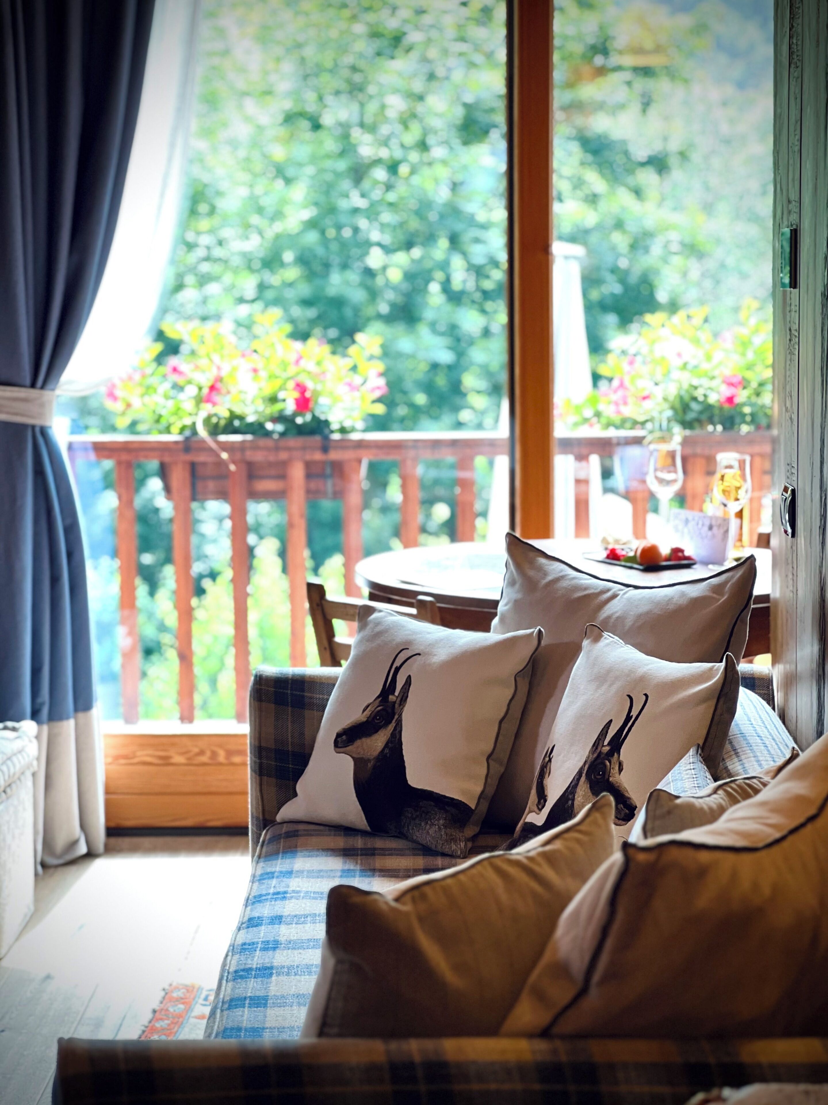 A cozy room with a sofa, pillows, and a view of a balcony with flowers.