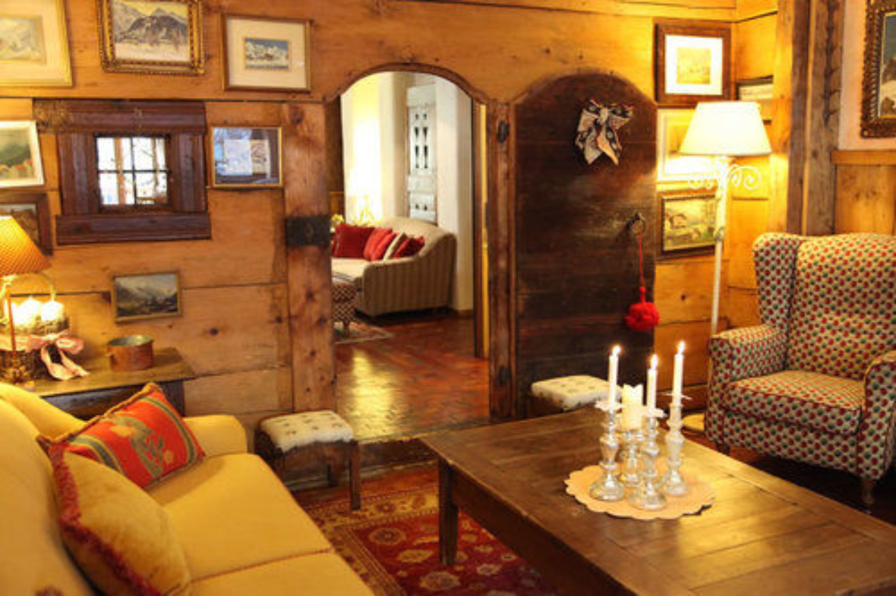 Un salon chaleureux avec un plancher en bois, un canapé jaune, un fauteuil à motifs et une table basse décorée de bougies.