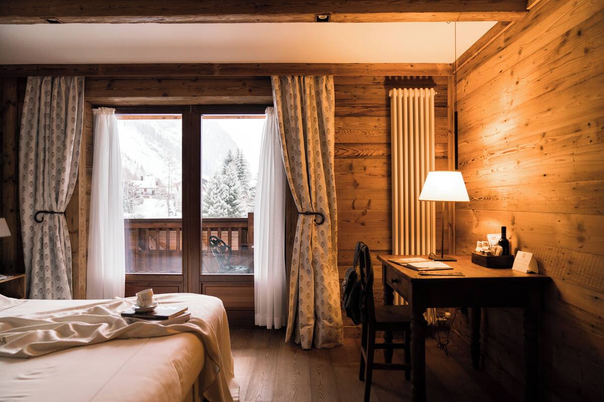 Acogedora habitación de cabaña de madera con una cama, un escritorio y una ventana con vistas a una montaña nevada.