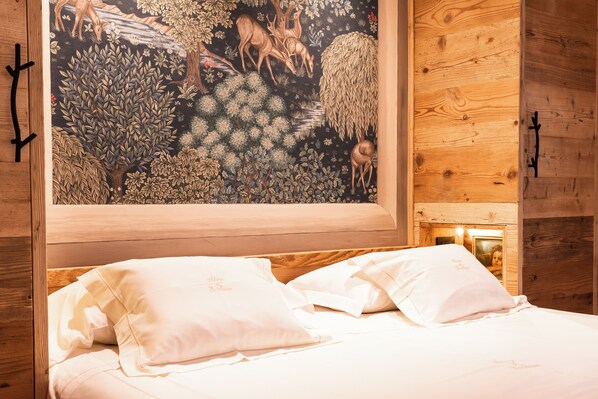 Habitación de cabaña de madera con una cama, ropa de cama blanca y un cuadro grande de ciervos y árboles en la pared.