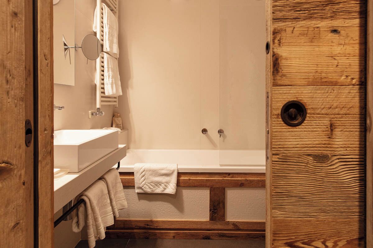 A bathroom with a wooden door, a white bathtub, and a sink with a mirror above it.