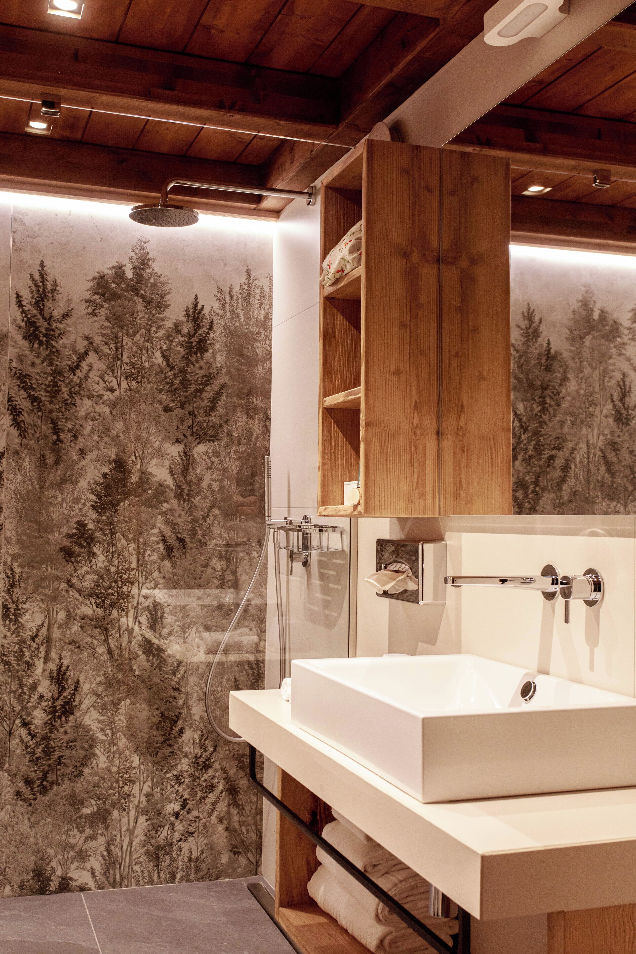 A bathroom with a large sink, wooden shelves, and a forest-themed wallpaper.