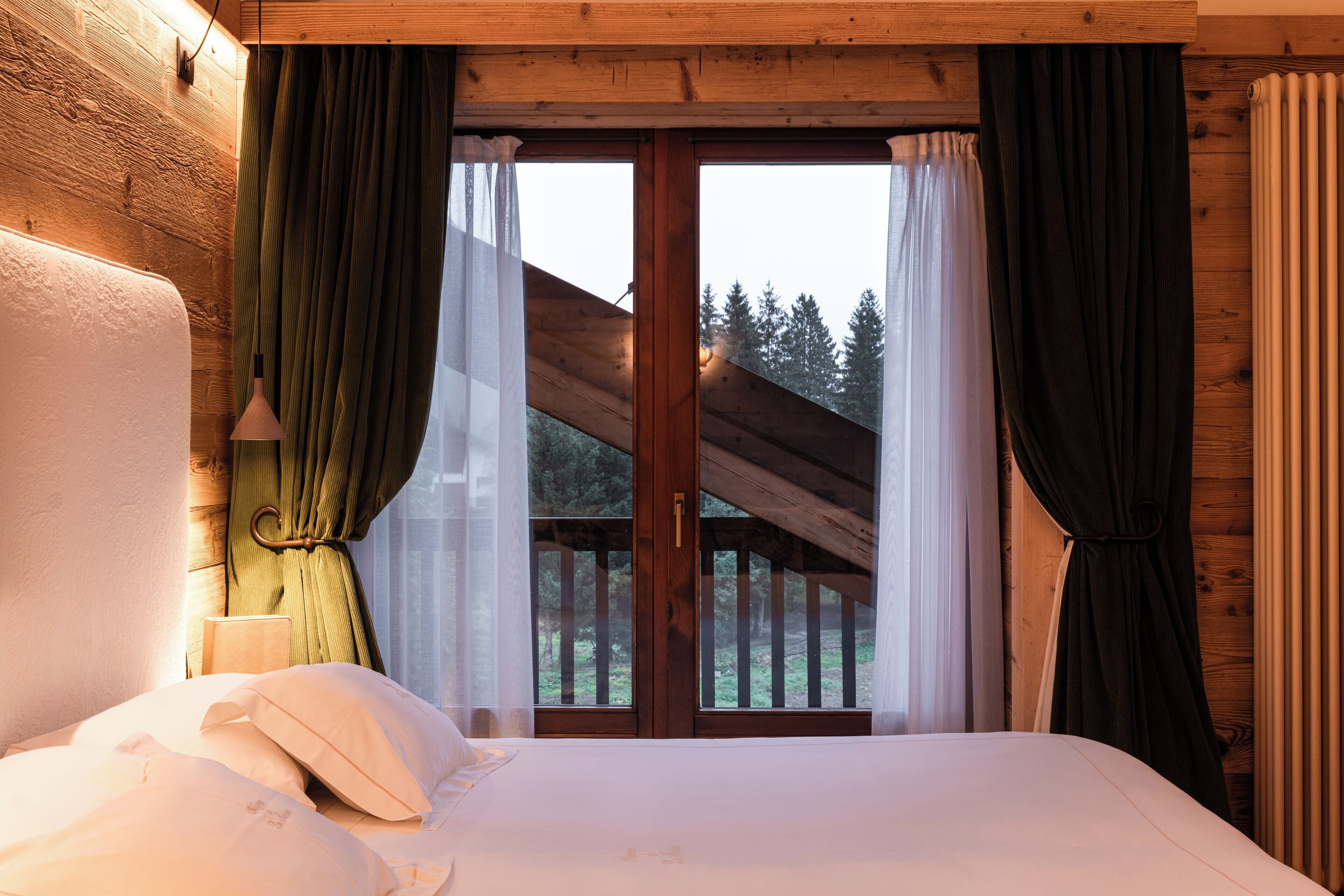 Un dormitorio con una cama grande, vigas de madera en el techo y vista a un bosque por una puerta de cristal.