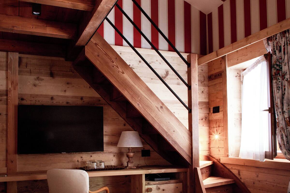 Interior de una cabaña de madera con una escalera, una cama, un escritorio y un televisor.