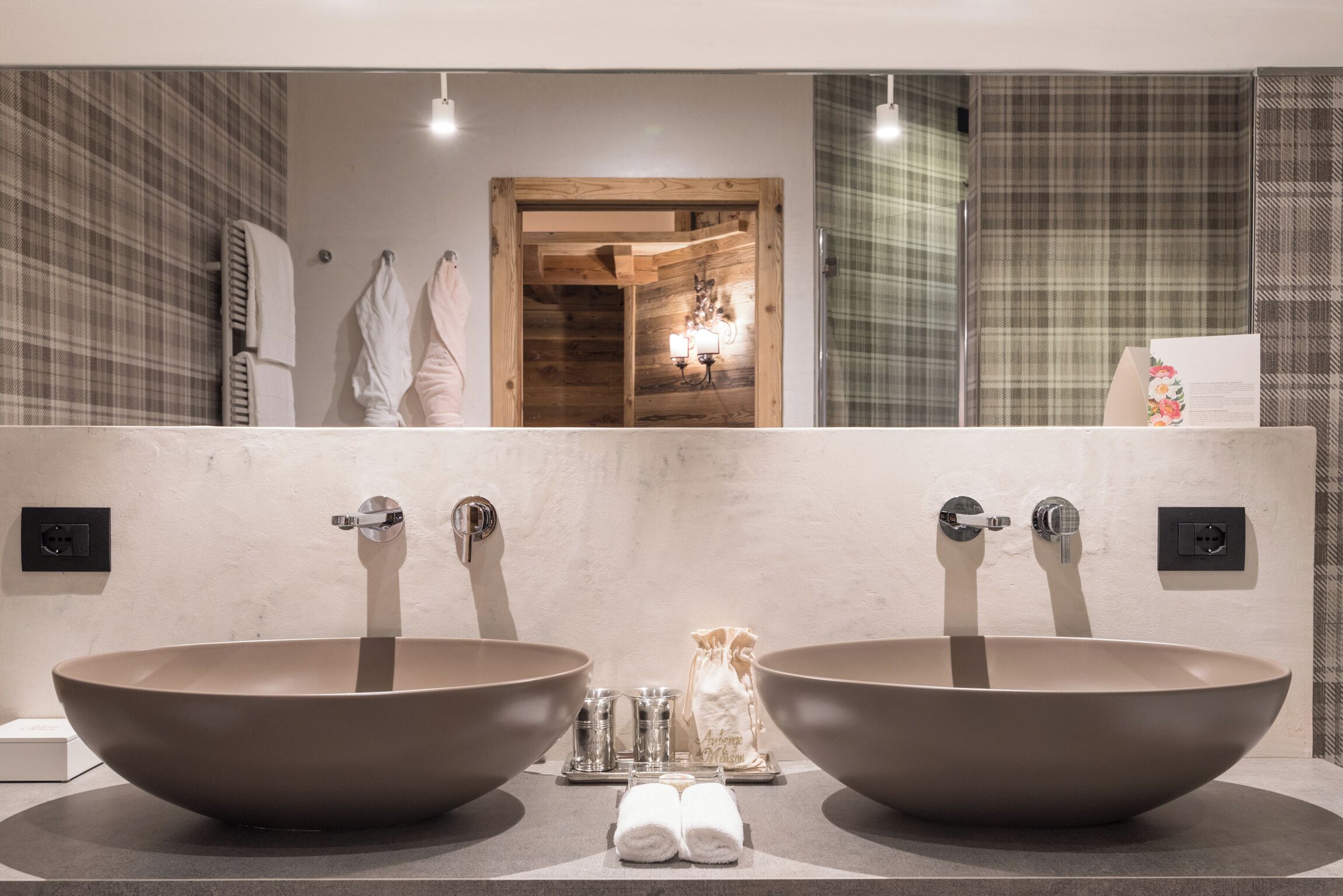 Une salle de bain avec deux grands lavabos ronds, un miroir et une porte en bois donnant sur l’espace de la douche.